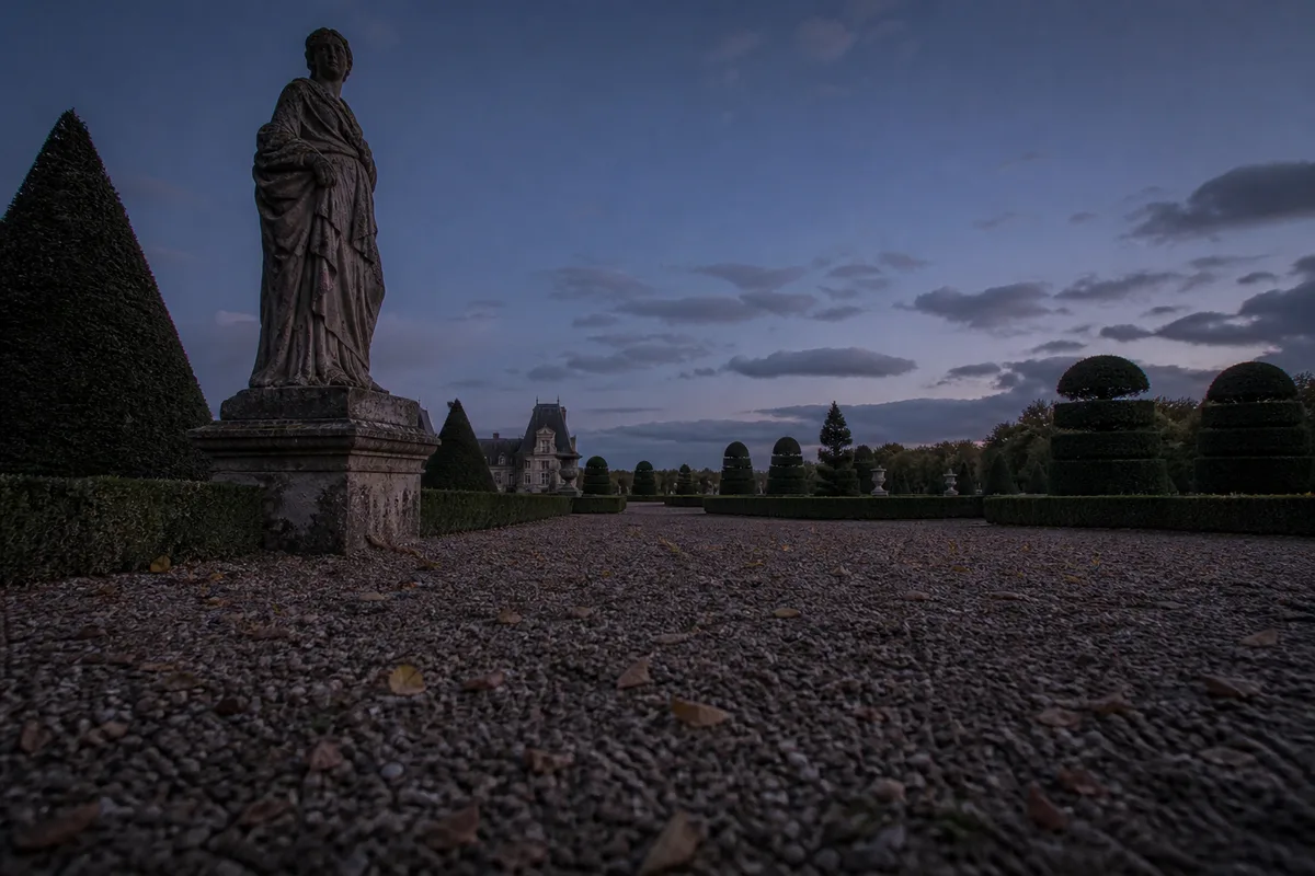 Parc à la française au crépuscule, statue de pierre et bosquets taillés
